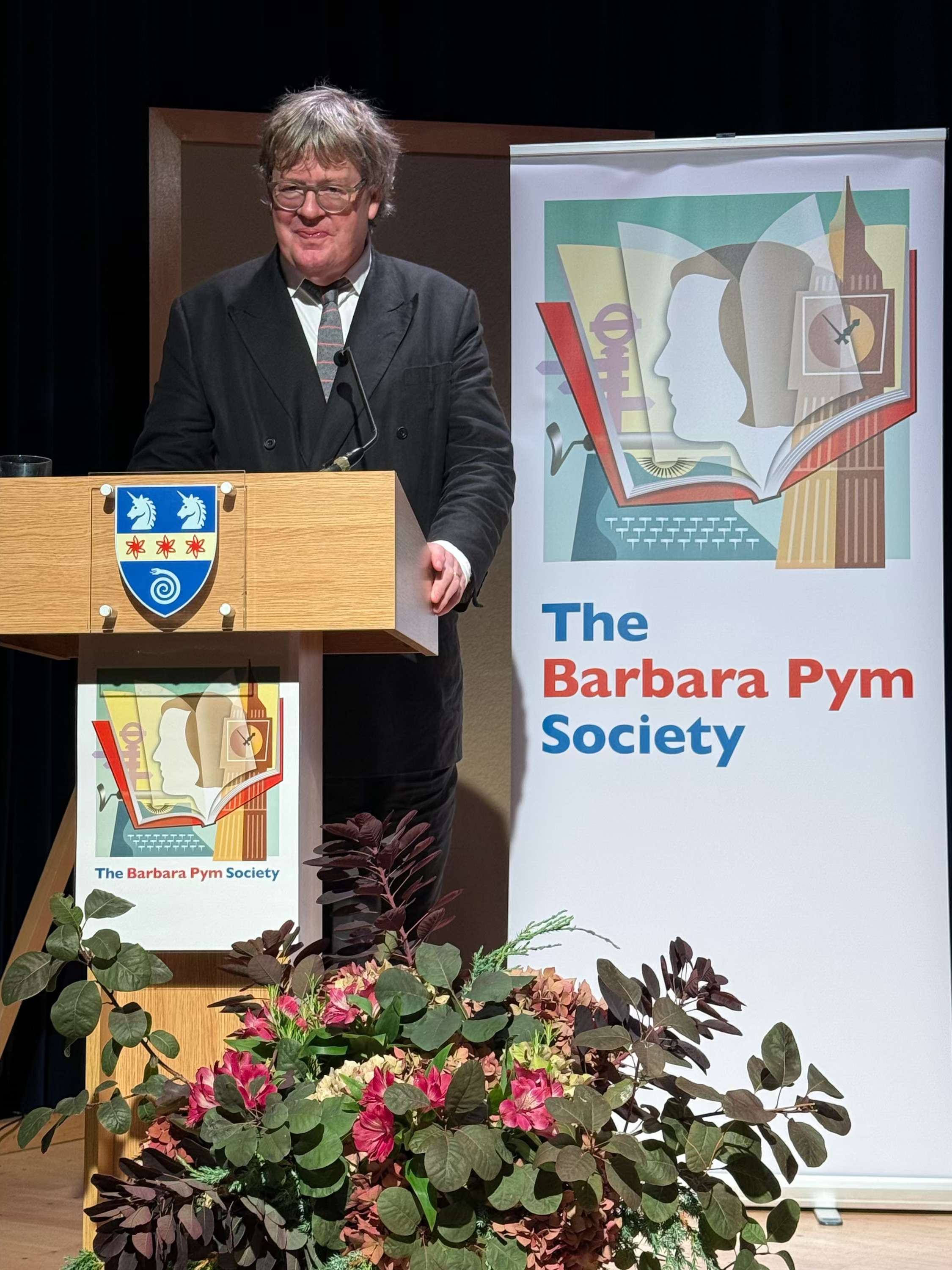 James Runcie giving the annual lecture at a lectern beside a Barbara Pym Society banner
