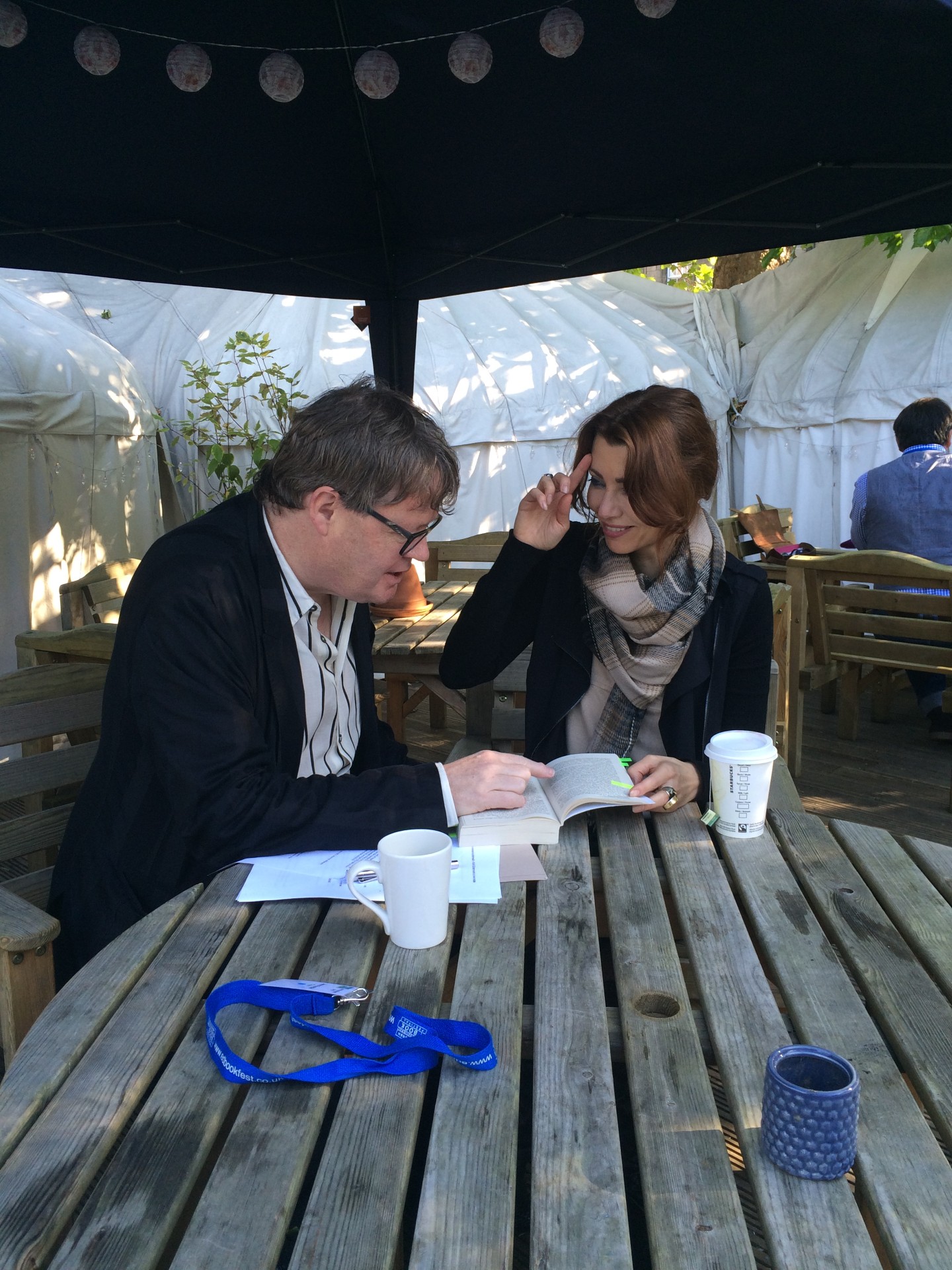 James Runcie reading a book at an outdoor festival table with author Elif Shafak