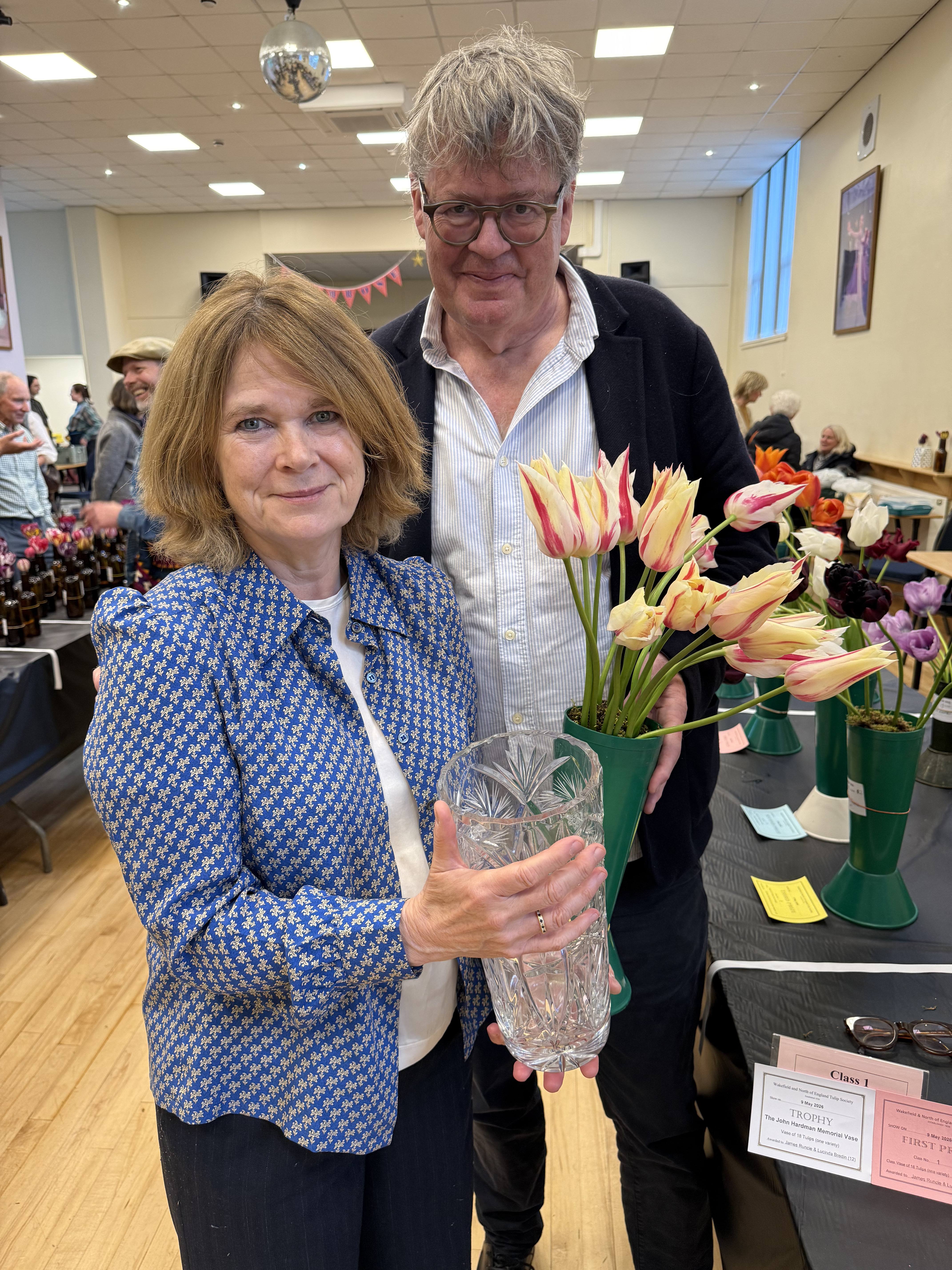 James Runcie and his wife Lucinda Bredin at a village tulip show, holding a crystal vase and a vase of flamed tulips